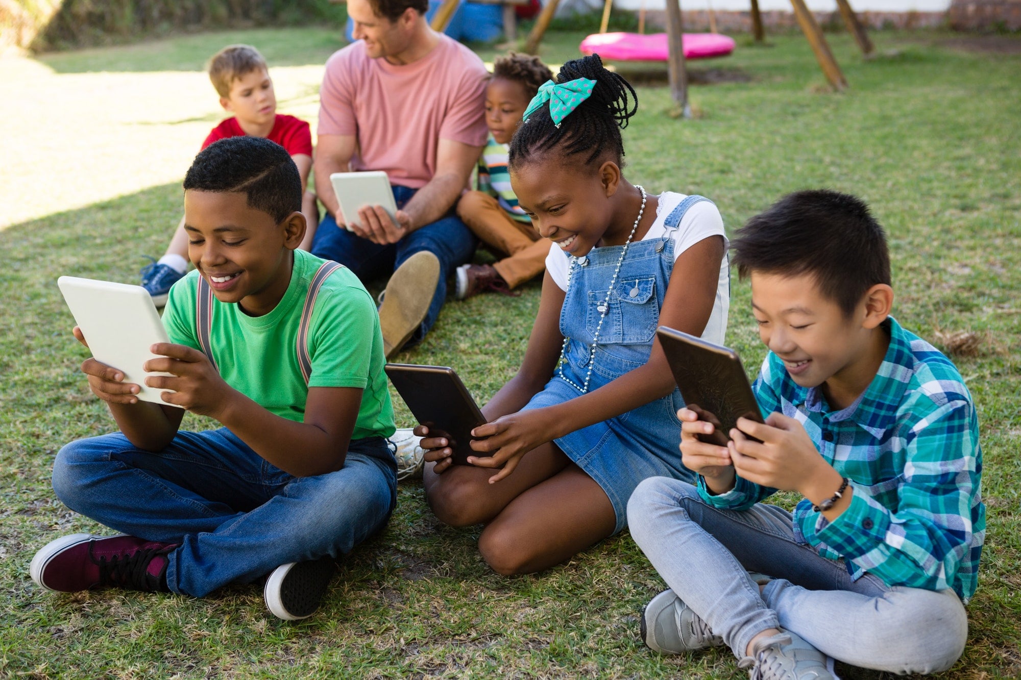 Children using tablet computer with man at park