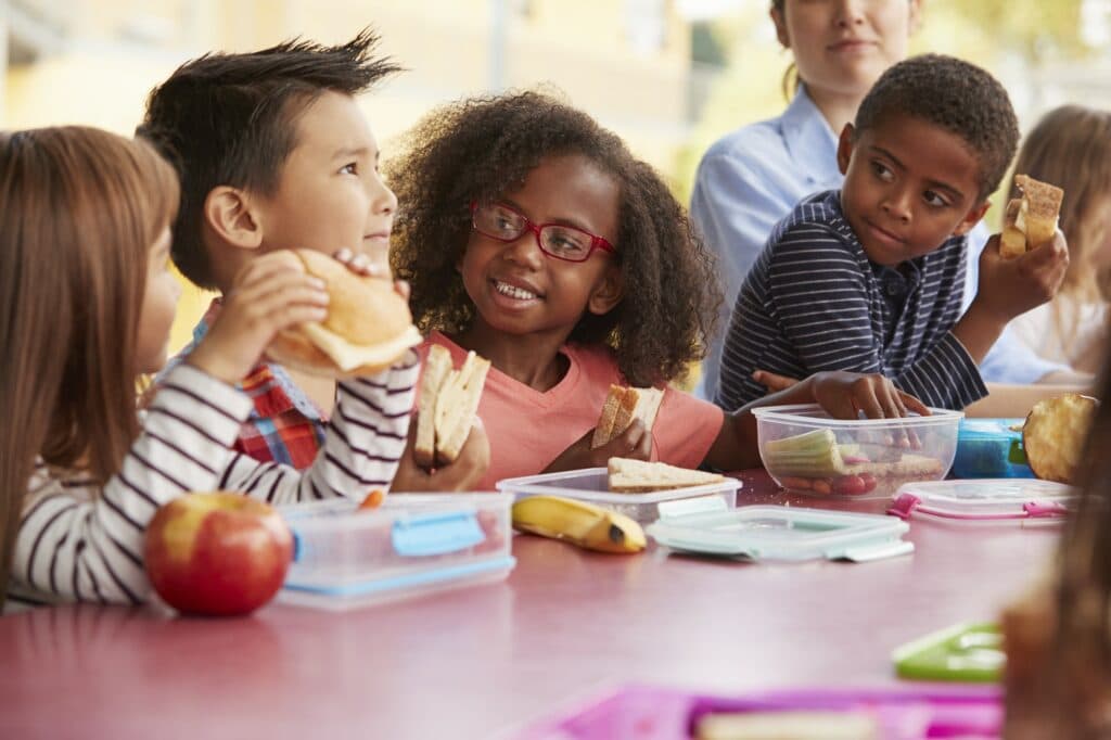 Young school kids eating lunch talking at a table together